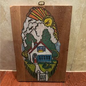 This is a small,hand-painted wooden plaque featuring a house and sun design.